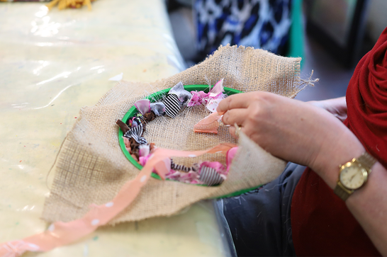 A person is weaving pink and purple material onto brown fabric