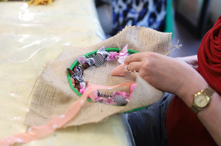 A person is weaving pink and purple material onto brown fabric