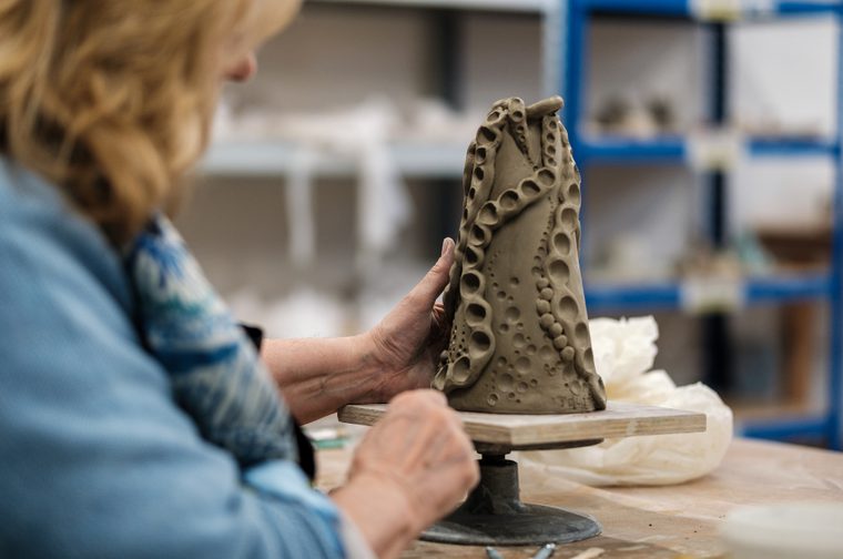 A woman is holding a clay vase, with circular shapes carved from it