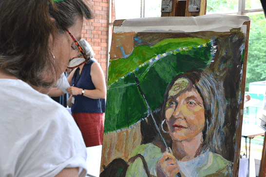 A woman is standing in front of a painting of a woman holding a green umbrella