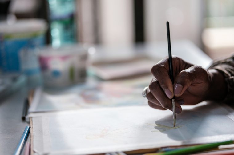 A hand holding a paint brush, painting onto a piece of paper.