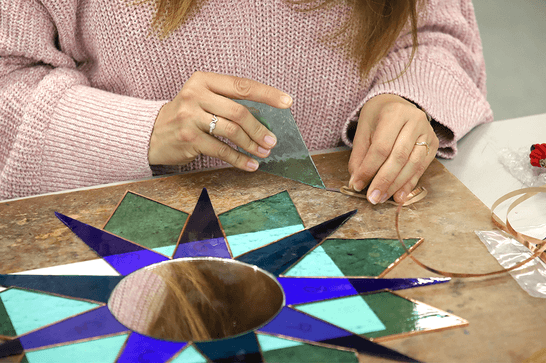 A person is attaching copper foiling to a triangle of light blue glass