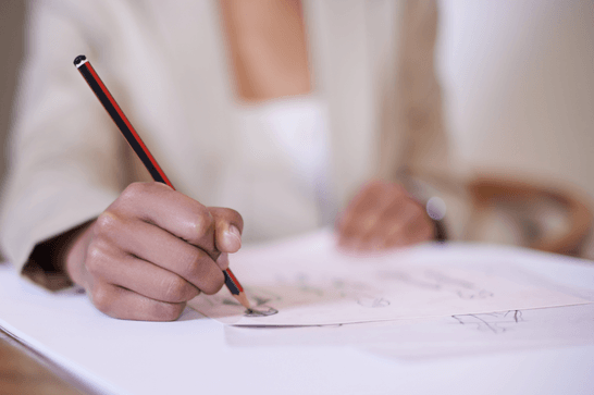A person is using a HB pencil to draw onto a black sheet of paper