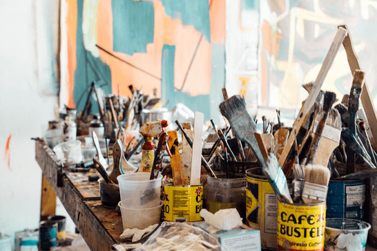 A table filled with art supplies, with tins filled with paint brushes