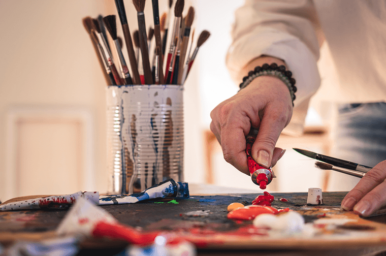 A person is squeezing out red oil paint from a paint tube