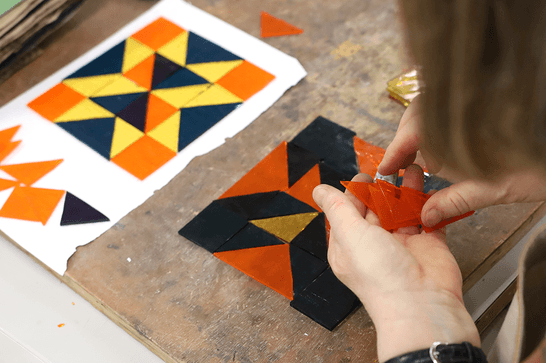 A person is holding orange glass triangles, arranging them into a pattern