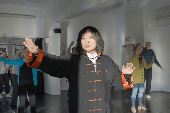 The teacher is at the front of the class, moving their hands into a tai chi position