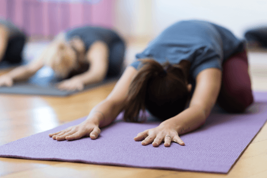 A person is in child's pose on a purple yoga mat