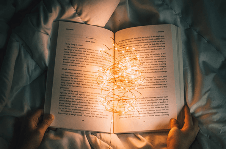 A book is open against some material, and fairy lights are placed in the centre of the book, lighting up the pages