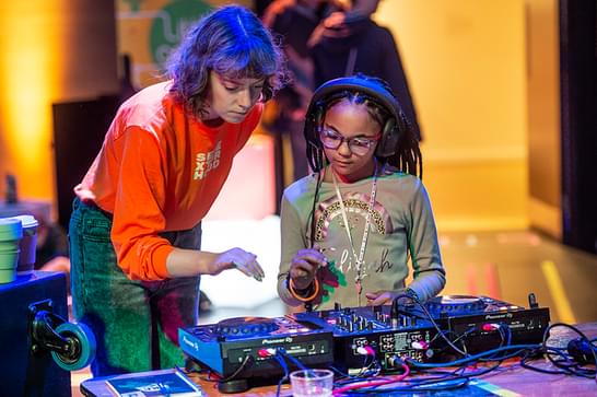 Young girl wearing headphones learning how to DJ with professional DJ