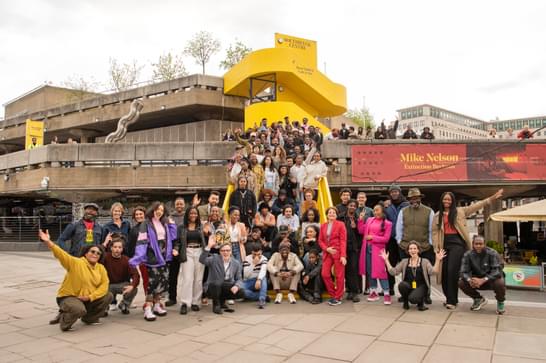 Group of Black and Black Mixed Heritage artists stand on the steps of the Southbank Centre with iconic yellow staircase