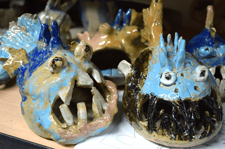 Ceramic fish made by children. They have been painted blue and black and have bit scary teeth.