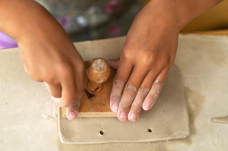 Close up of a child's hands printing a stamp into a rectangular piece of clay.