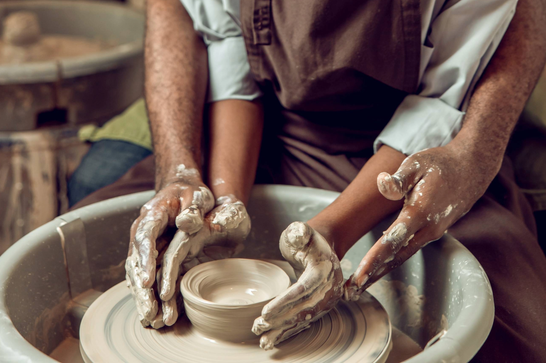 Two hands are moulding a bowl that is on a pottery wheel