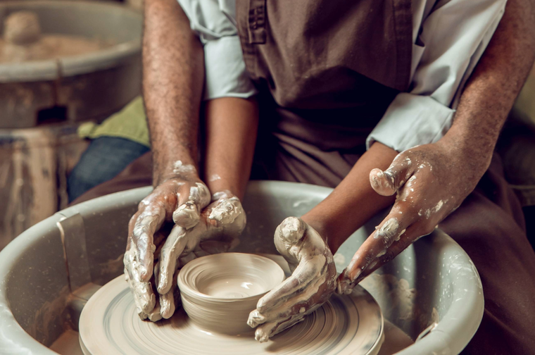 Two hands are moulding a bowl that is on a pottery wheel