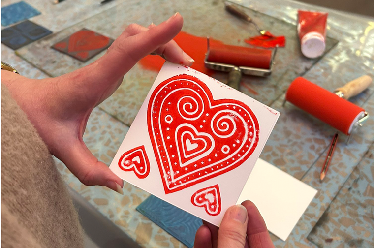 A person is holding a square piece of white card, with a decorative heart printed in the middle