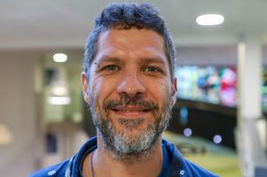 A man with dark hair and a beard, who is smiling at the camera
