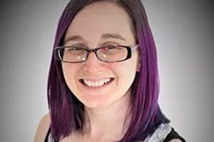 Helen is sat against a white background and has purple hair. Helen is wearing a black tank top and glasses.