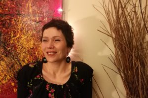 ILdiko has short brown hair and is wearing a floral top and circular earrings.