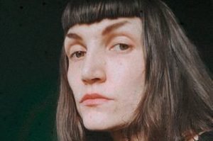 Kat is sitting down, with long brown hair and a fringe.