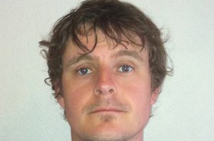 Peter has short brown hair and is stood against a white background.