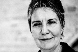 Polly has short brown hair and is wearing a black blazer.