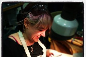 Vanessa Miller has long brown hair and a fringe, and is seated at a jewellery table filing down metal
