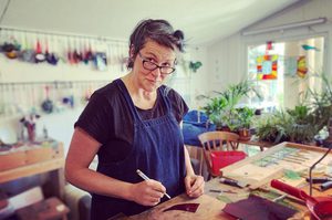 Victoria Brown is at a crafting station, wearing a blue apron and glasses