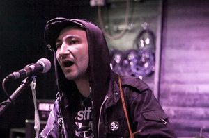 Niall is wearing a jacket, hoodie and hat and is playing the guitar and singing into a microphone.