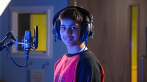 A young person smiling in MAC's recording studio with headphones on