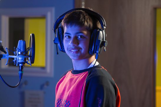 A young person smiling in MAC's recording studio with headphones on