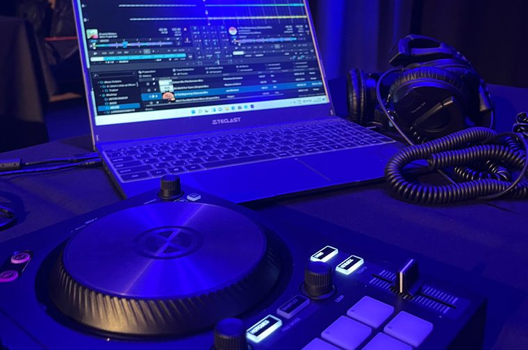 A set of DJ decks to the left, to the right there is a laptop showing a music editing software, that is beside some black headphones