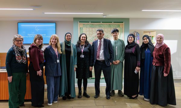 Image shows a group of people standing in a line in front of a textile mural.