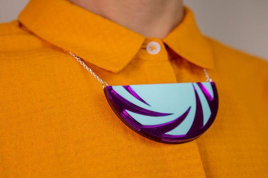 Orange blouse with bright semi-circle necklace with blue and purple design.