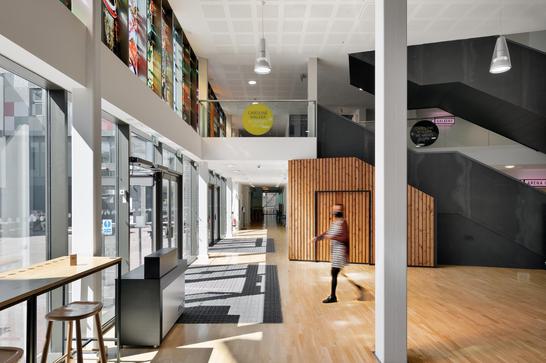 Building with big glass windows and sun shining through. Woman walks across floor.