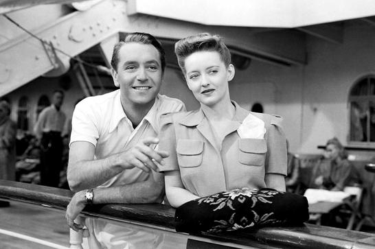 Black and white photo of a man and a woman (Bette Davis) standing on a dock next to a cruise liner. The main points off camera.