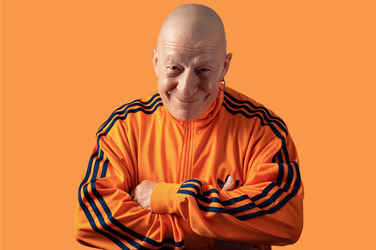 A man wearing an orange tracksuit smiling with his arms crossed.