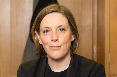 MP Jess Phillips looks straight forward in front of a wooden panneled wall- she has light brown hair and is wearing a black blazer jacket.