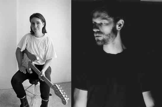 On the left a guitarist - Jessica Ackerley - with long dark hair wearing a white tshirt sits on a stool. On the right Eli Wallace wears a black tshit and has dark stubble.