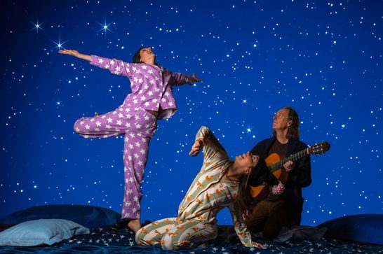 Two people dance against a background of a starry night, with a person playing guitar next to them
