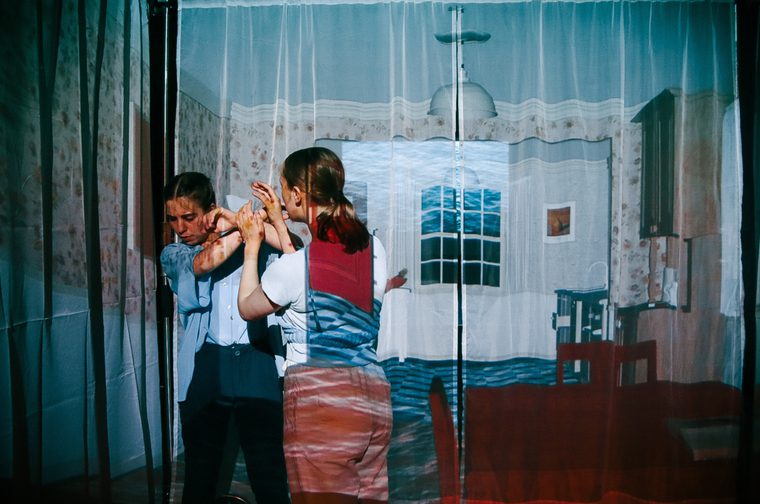 Two people dancing in a room with layered transparent curtains creating a dreamlike, multi-dimensional visual effect.