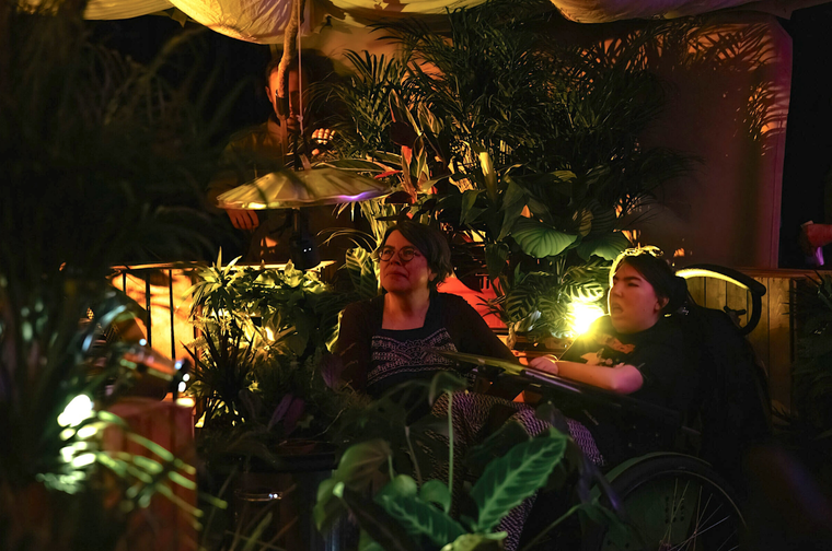 Two women in a dimly lit theatre space. It is designed to look like a magical rainforest and is a sensory space.