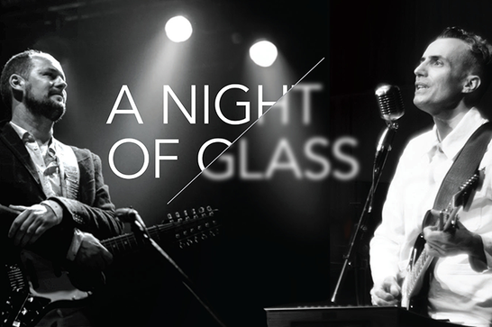 Black and white - two men with guitars face each other, one is playing and the other has crossed his arms. The text "A Night Of Glass" is in the centre below two spotlights.