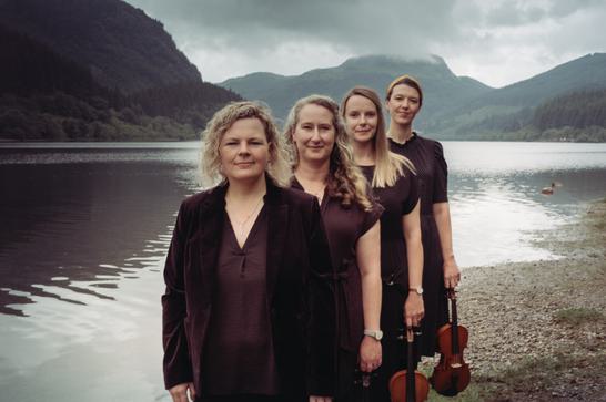 The 4 members of RANT stand in front of a lake with mountains in the background.