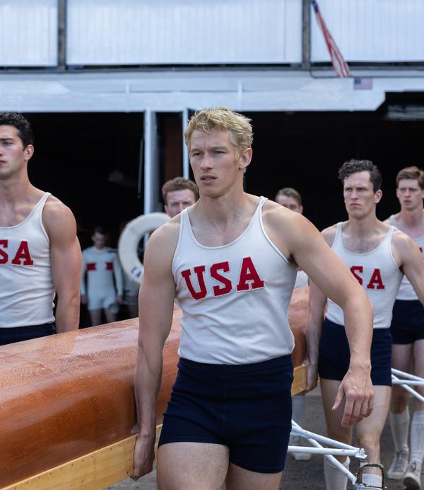 A group of young men in white vests with the red letters USA printed on them carry an orange rowing boat.