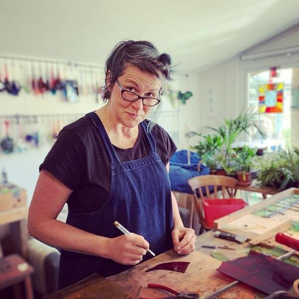 Victoria Brown is at a crafting station, wearing a blue apron and glasses