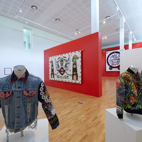 Install shot of a gallery with big red wall and jackets with embroidery