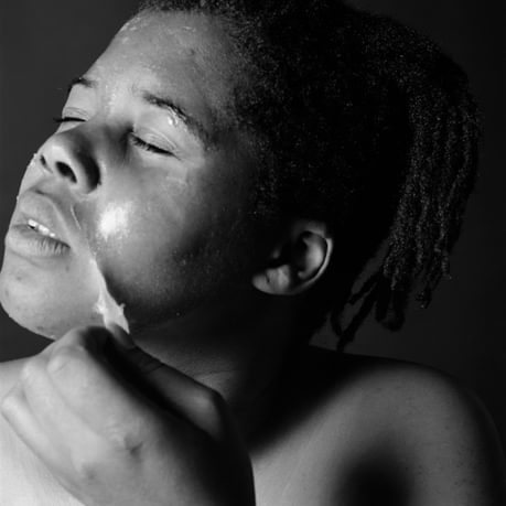 Photograph of artist Maxine Walker, closed eyes and turned away from camera, peeling something from her facial skin.
