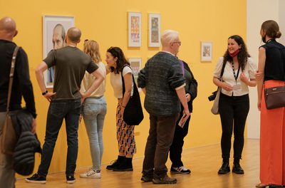 People in various poses attending an exhibition launch in front of a bright yellow room