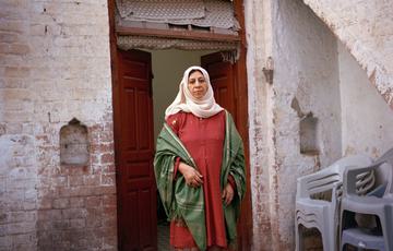 Woman in red saree and white hijab standsin front of a Pakstani building smiling at the camera